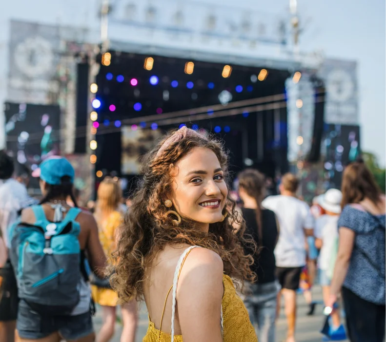 Woman at a music festival with a crowded stage and colorful lights in the background